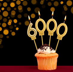Birthday candle with cupcake - Number 6000 on black background with out of focus lights