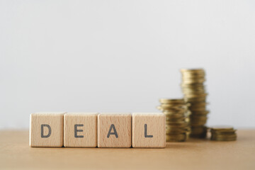 DEAL text on wooden cabe blocks with blurred stack of coins including copy space
