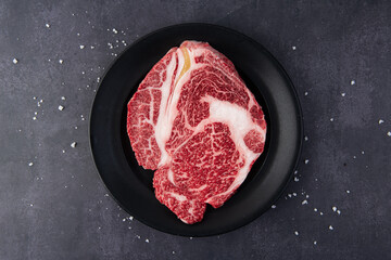 Raw fresh marbled beef steak on black plate with sea salt, top view
