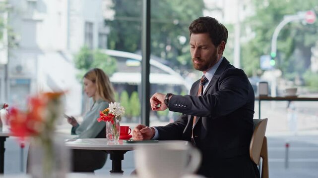 Serious businessman checking time at hand watch sitting cafe. Man waiting 