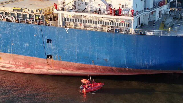 Aerial View of Cargo Ship Crew in Small Skiff Boat Making Repairs to Ship