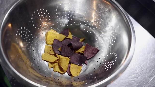 Gold and red corn chips are dropped slo mo into steel colander