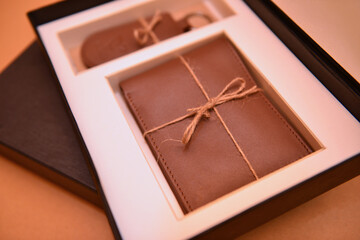 A closeup of a new natural brown leather wallet and key ring in black box on beige background
