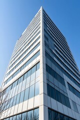 Obraz premium A modern, sleek skyscraper with large glass windows, set against a clear blue sky, showcasing contemporary architectural design.