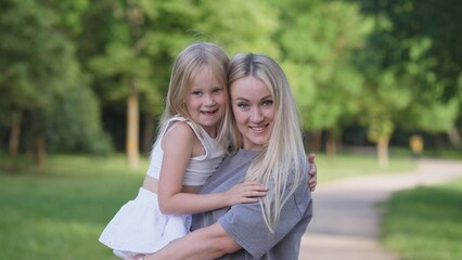 Fototapeta premium In a lush green park setting, a joyful mother is embracing her beloved daughter with love and warmth