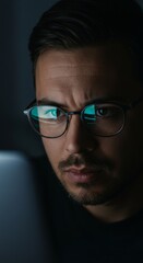 Obraz premium Close-up of a man with glasses reading news on a laptop in the dark