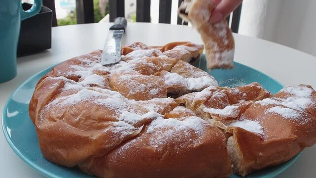 Fluffy chocolate-filled Ensaimada on a plate with powdered sugar, knife on the side