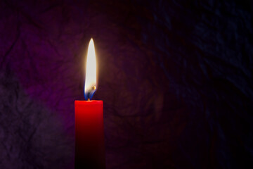 Red candle with flickering flame against a textured dark background