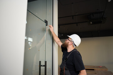 Bearded worker installing glass door in the new office. Construction worker installing door in a...