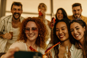 Obraz premium Group of cheerful friends taking selfie while eating pizza at a party