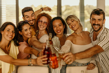 Group of cheerful friends toasting with bottles and glasses during a party