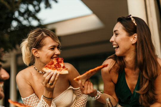 Two happy women eating pizza and having fun together at a restaurant