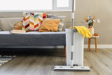 Cleaning supplies: mop, gloves, bucket with wringer sitting on wooden laminate floor in modern...