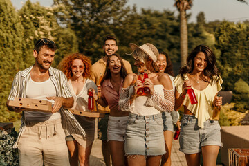 Cheerful people carrying pizza and drinks laughing together at a party