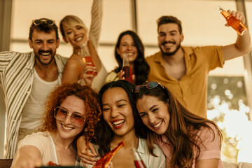 Fototapeta premium Group of diverse cheerful friends taking selfie while eating pizza at a party