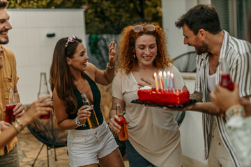 Diverse friends surprising redhead woman with birthday cake and lit candles