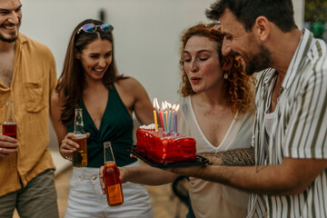 Group of friends holding birthday cake with lit candles, laughing and celebrating