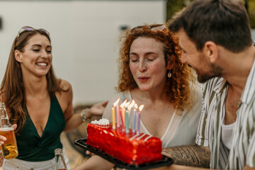 Group of friends holding birthday cake with lit candles, laughing and celebrating