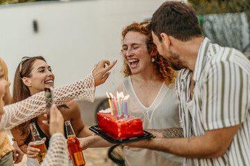 Group of friends holding birthday cake with lit candles, laughing and celebrating