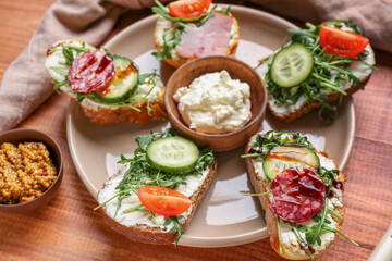Plate with delicious sandwiches, cream cheese and mustard on wooden table, closeup