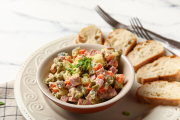 Bowl of tasty Olivier salad on white marble background