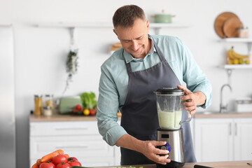Mature man making smoothie with blender in kitchen