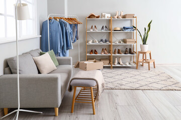 Interior of light boutique with shelving unit, sofa, rack, stylish clothes and shoes