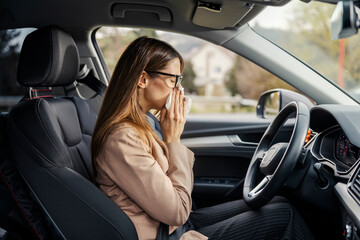 Side view of sick female driver having cold and blowing her nose with tissue.