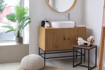 Sink bowl and bath accessories on wooden cabinet in interior of light bathroom