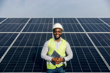 Portrait of interracial photovoltaic power station engineer standing near solar panels with tablet...