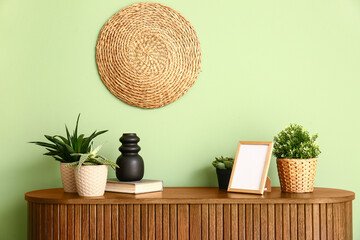 Green houseplants with frame on chest of drawers near color wall