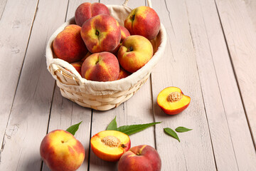 Wicker basket with sweet peaches and leaves on white wooden background