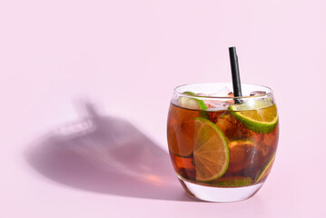 Glass of cold Cuba Libre cocktail on lilac background