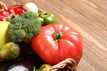Wicker basket with fresh ripe vegetables on wooden background, closeup