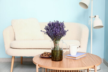 Jug with beautiful lavender flowers, tasty cookies and cup of coffee on table in living room, closeup