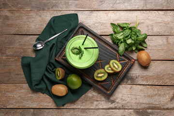 Board with glass of fresh kiwi smoothie and basil on wooden background