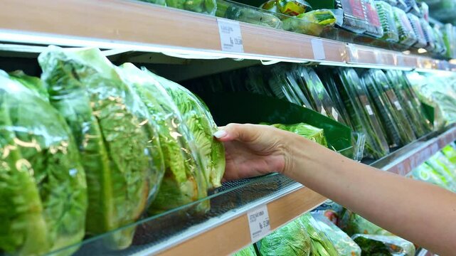 Consumer hand picking fresh salad in store facing plastic wrap dilemma Salad in plastic packaging raises environmental concerns Salad choice reflects conflict between convenience and sustainability
