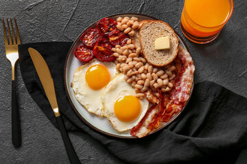 Plate with tasty English breakfast and glass of juice on black background