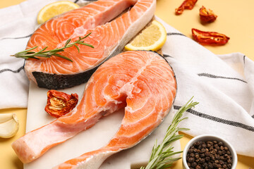 Board with raw salmon steaks and different spices on yellow background