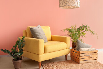 Stylish yellow armchair with cushion and houseplants near color wall