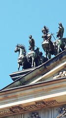 Obraz premium Bronze sculptures on roof, horse-drawn chariot, blue sky background, historical art concept