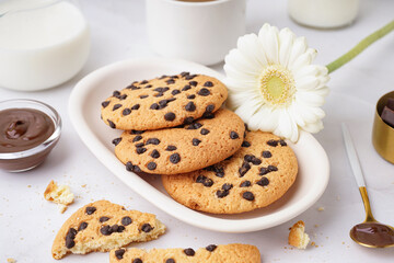 Plate of tasty cookies with chocolate chips and chamomile flower on white background