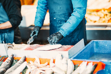 A fishmonger in protective gear cleans and prepares fresh fish at an outdoor seafood market. The detailed process highlights the trade, freshness, and craftsmanship of seafood preparation.