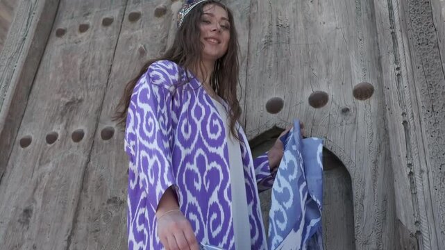 A young woman with long hair in a short white dress and an oriental robe against the background of a wooden gate
