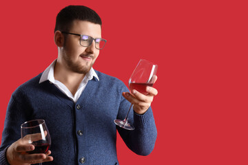 Young sommelier holding glasses with different types of wine on red background