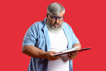 Afraid mature man with notebooks on red background