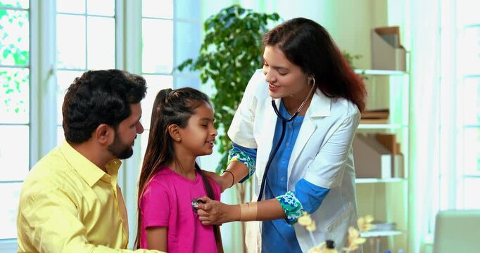 Indian Asian playful female doctor or pediatrician engaging young girl patient by letting her hear own heartbeat using stethoscope in a warm and friendly clinic atmosphere