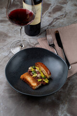 A gourmet European cuisine dish is beautifully arranged on a dark plate, complemented by a glass of red wine. Soft lighting enhances the intimate dining atmosphere