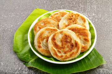 Middle eastern flat bread variety : ghee - glazed paratha on a banana leaf background.