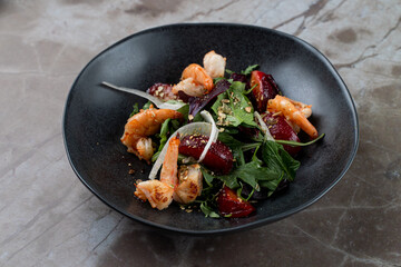 A vibrant seafood salad is served in a stylish bowl, showcasing succulent shrimp atop a bed of fresh greens. The ambiance is elegant and contemporary and enhances the dining experience